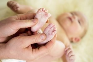 father or doctor massaging small baby feet